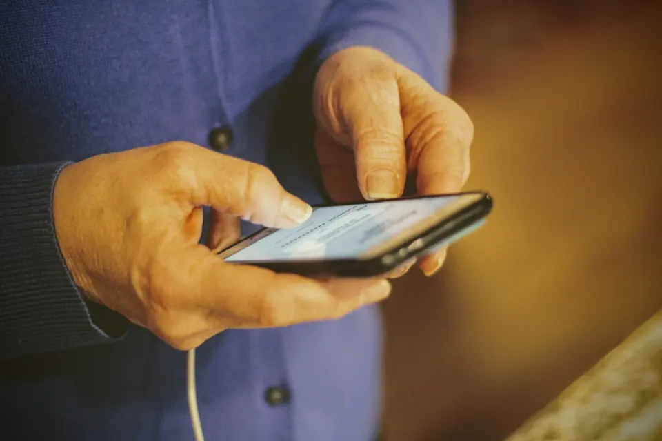 Eldre hender som holder en mobiltelefon som lades