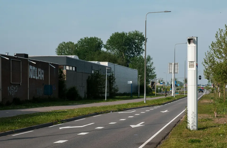 Hvit fotoboks på en stolpe ved siden av en vei med veimerking