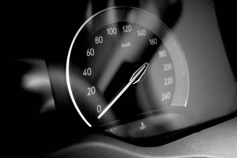 Svart-hvitt nærbilde av en speedometernål på vei oppover km/t-skalaen