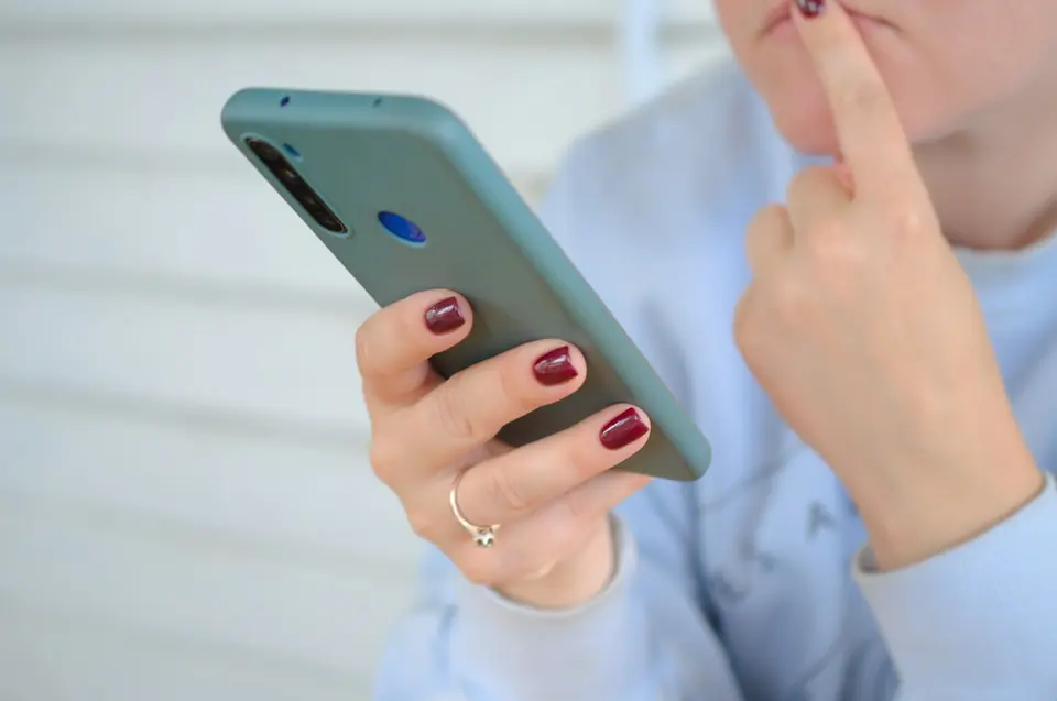 Kvinne ser ettertenksomt på mobilen hun holder i hånden