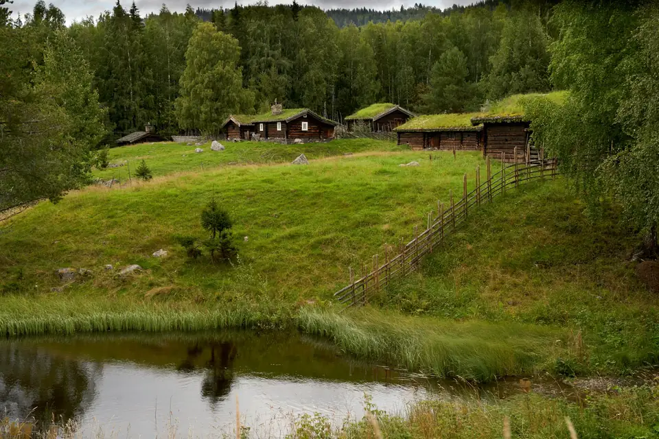 Gamle tømmerhus med torvtak og skigard ved en dam på Maihaugen i Lillehammer