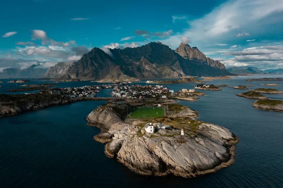 Fiskeværet Henningsvær i Lofoten sett fra lufta med fotballbane, holmer og takkete fjell